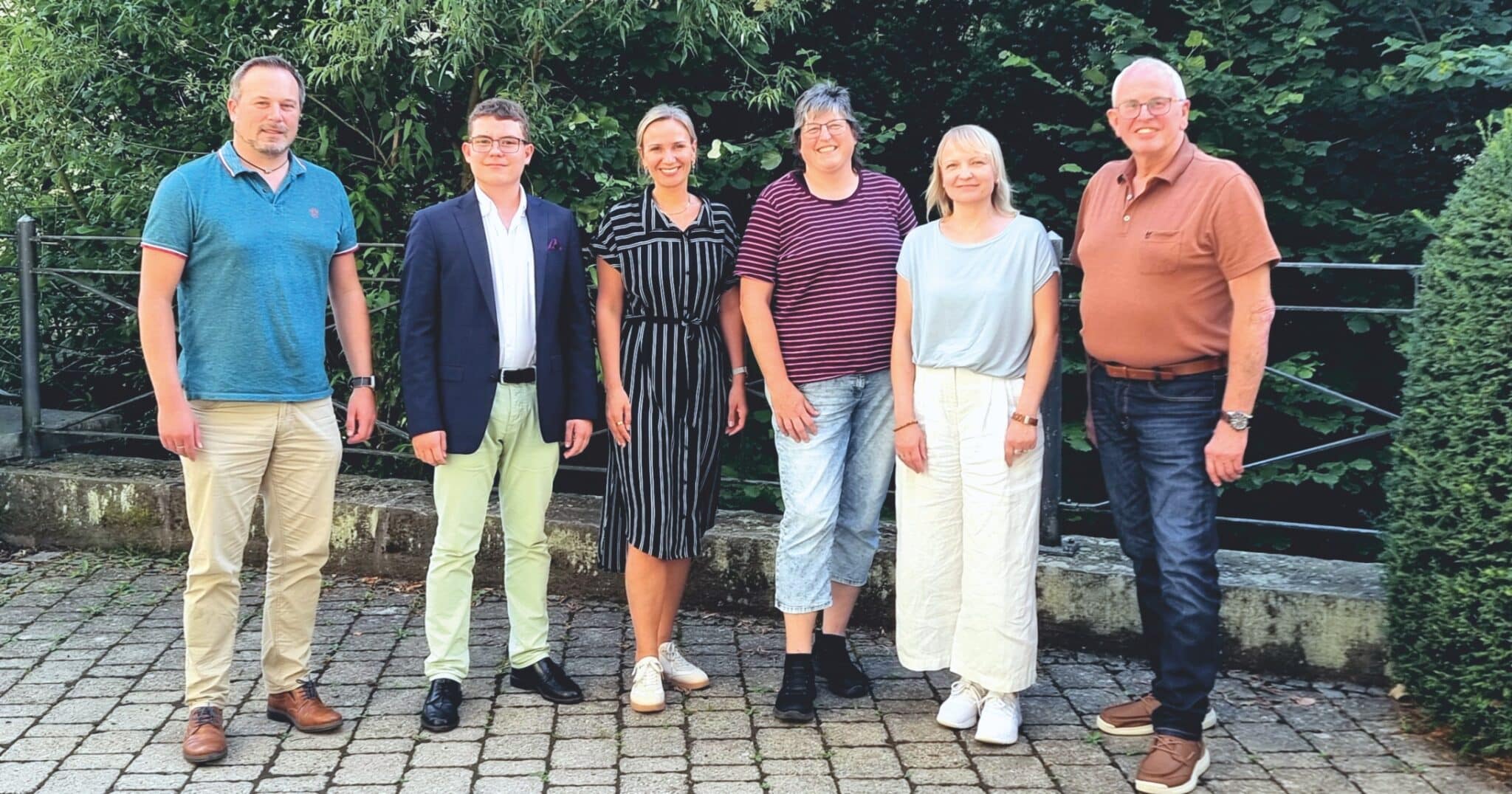 Eine Gruppe von Menschen in Alltagskleidung stehen nebeneinander und lächeln in die Kamera.